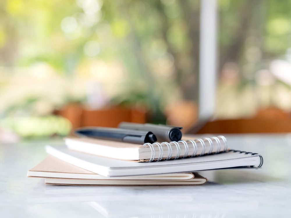 Books and notebooks with pens on the table with blur green nature background