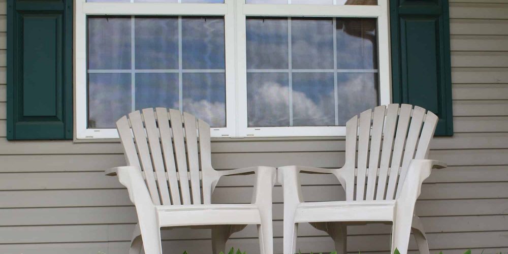 Chairs on a porch with the sky reflecting in the windows
