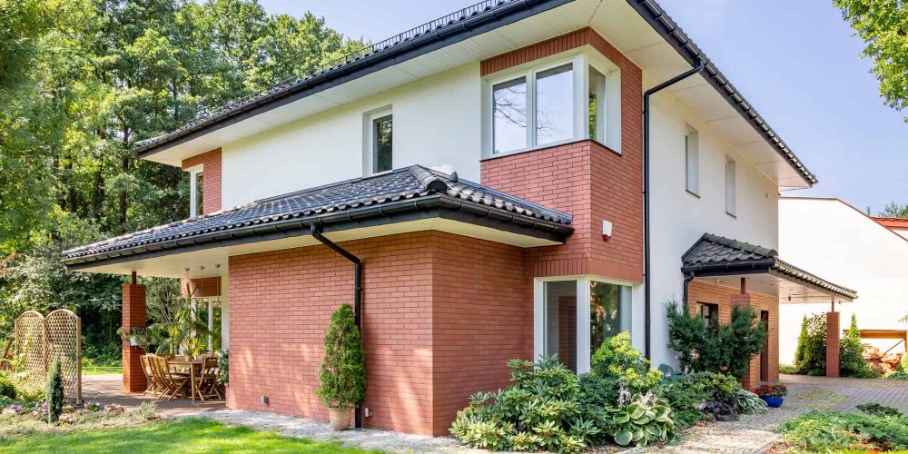 Red brick house with terrace and green grass and trees during su