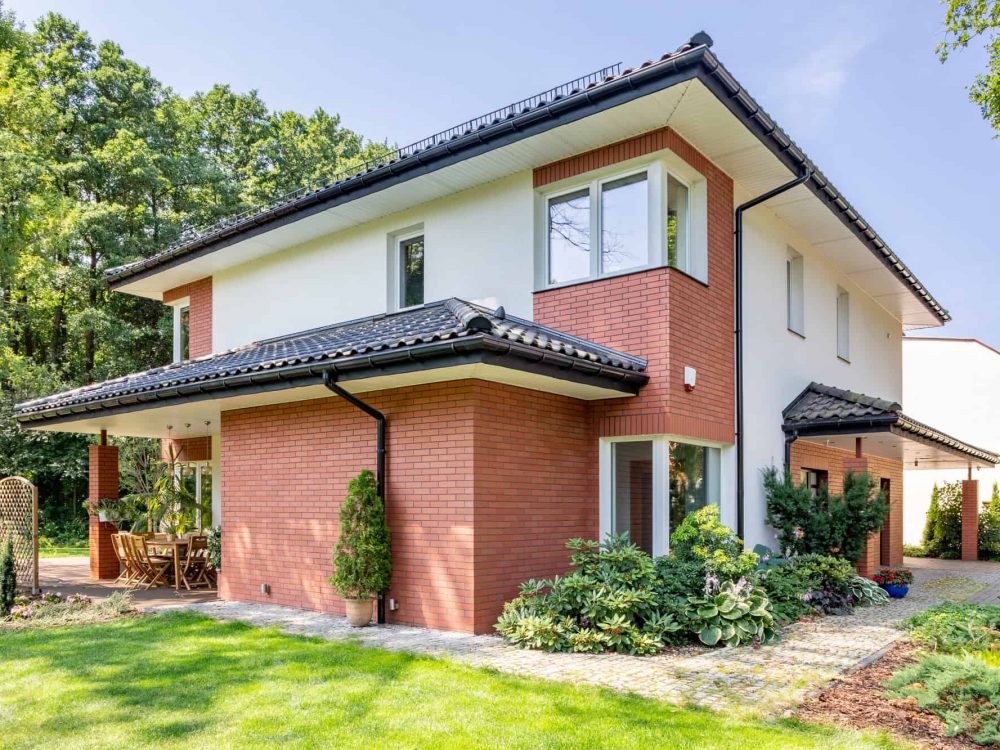 Red brick house with terrace and green grass and trees during su